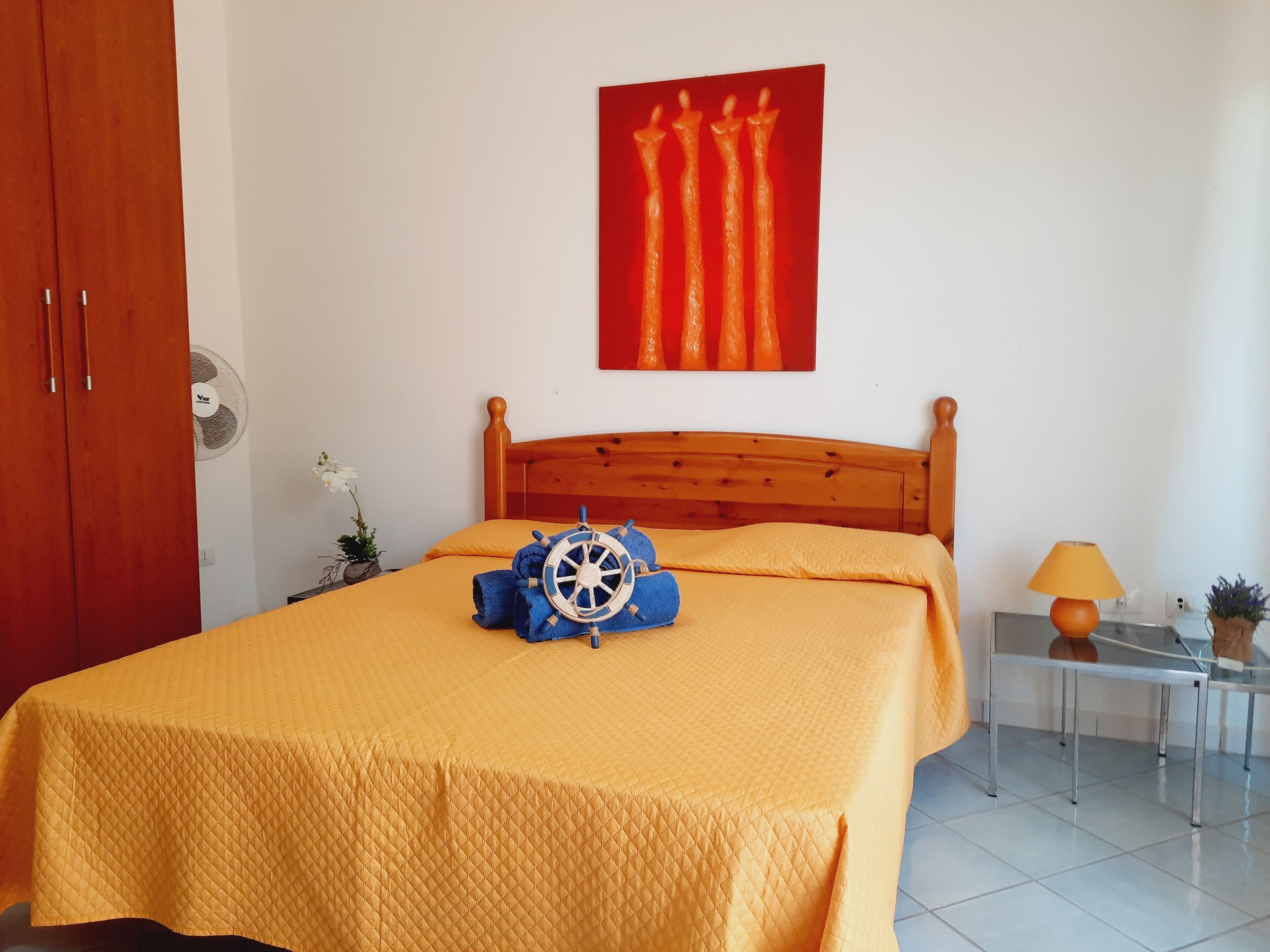 Une chambre avec un lit en bois, une œuvre d’art rouge accrochée au mur, une table de chevet avec une lampe et une petite plante.