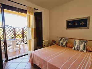 Une chambre à coucher comprenant un lit, une table de chevet, une fenêtre avec des rideaux et une vue sur le balcon extérieur.