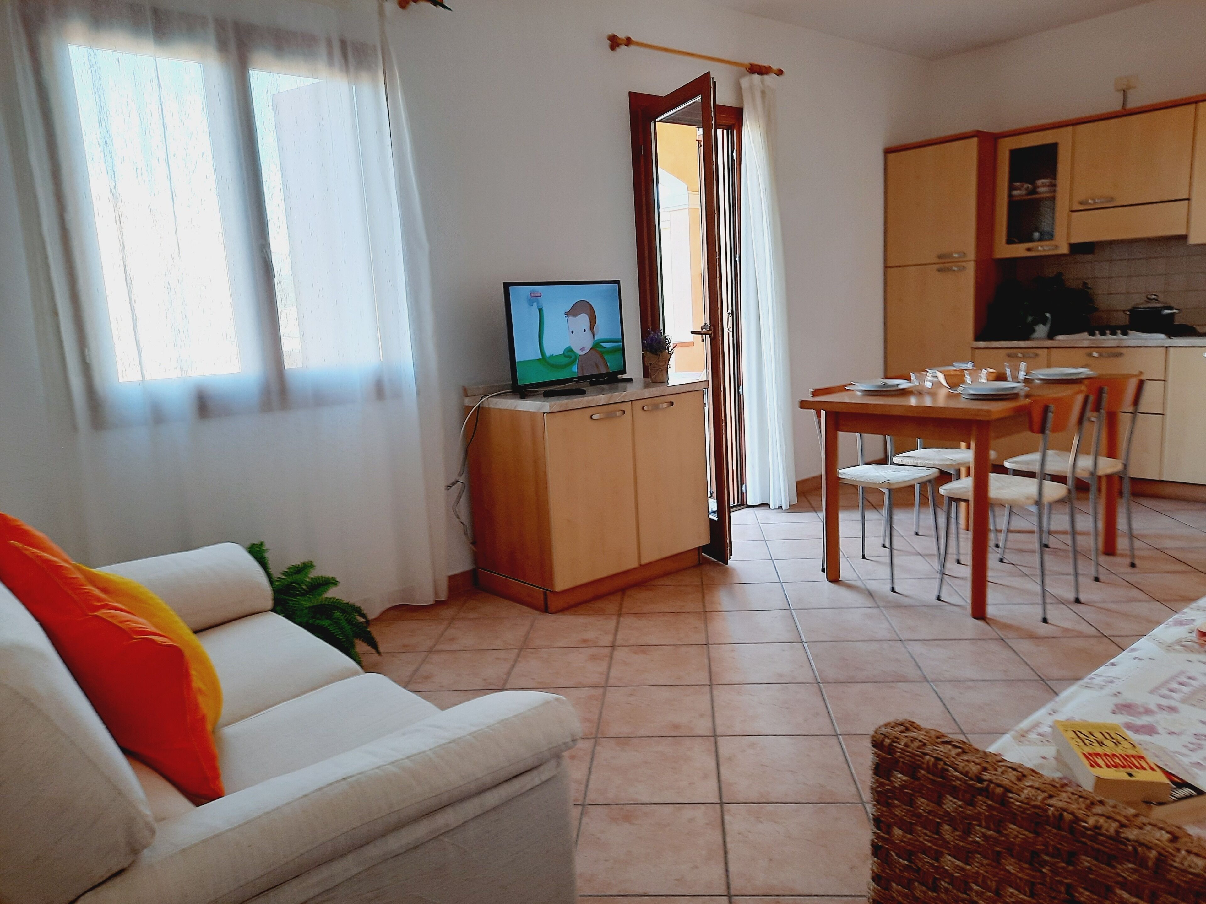 A living room with a sofa, a television, a dining table with chairs, and a kitchen area with cabinets.
