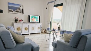 A living room with two grey sofas, a white cabinet, a TV, and a view of the outdoors through a window. - Appartamenti Santa Teresa Gallura (Santa Teresa di Gallura)