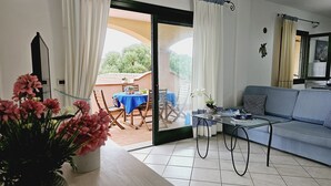 A living room with a sofa, a glass coffee table, and a dining table with chairs. There is a sliding glass door leading to an outdoor area with a table and chairs. - Appartamenti Santa Teresa Gallura (Santa Teresa di Gallura)