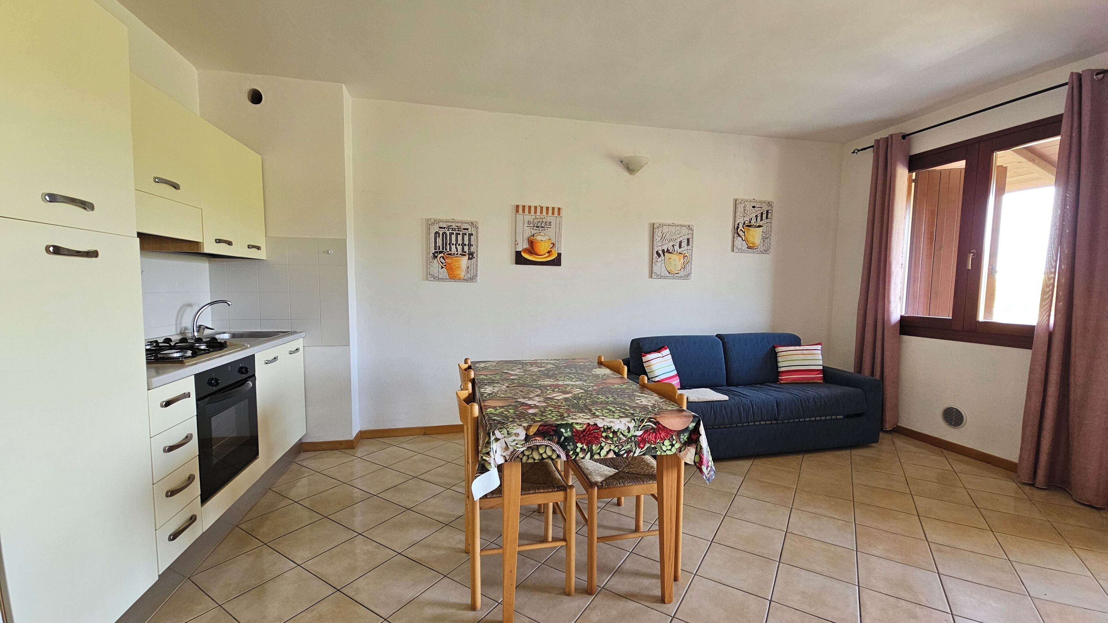 A compact kitchen with a dining table and chairs, a sofa, and a window with curtains.