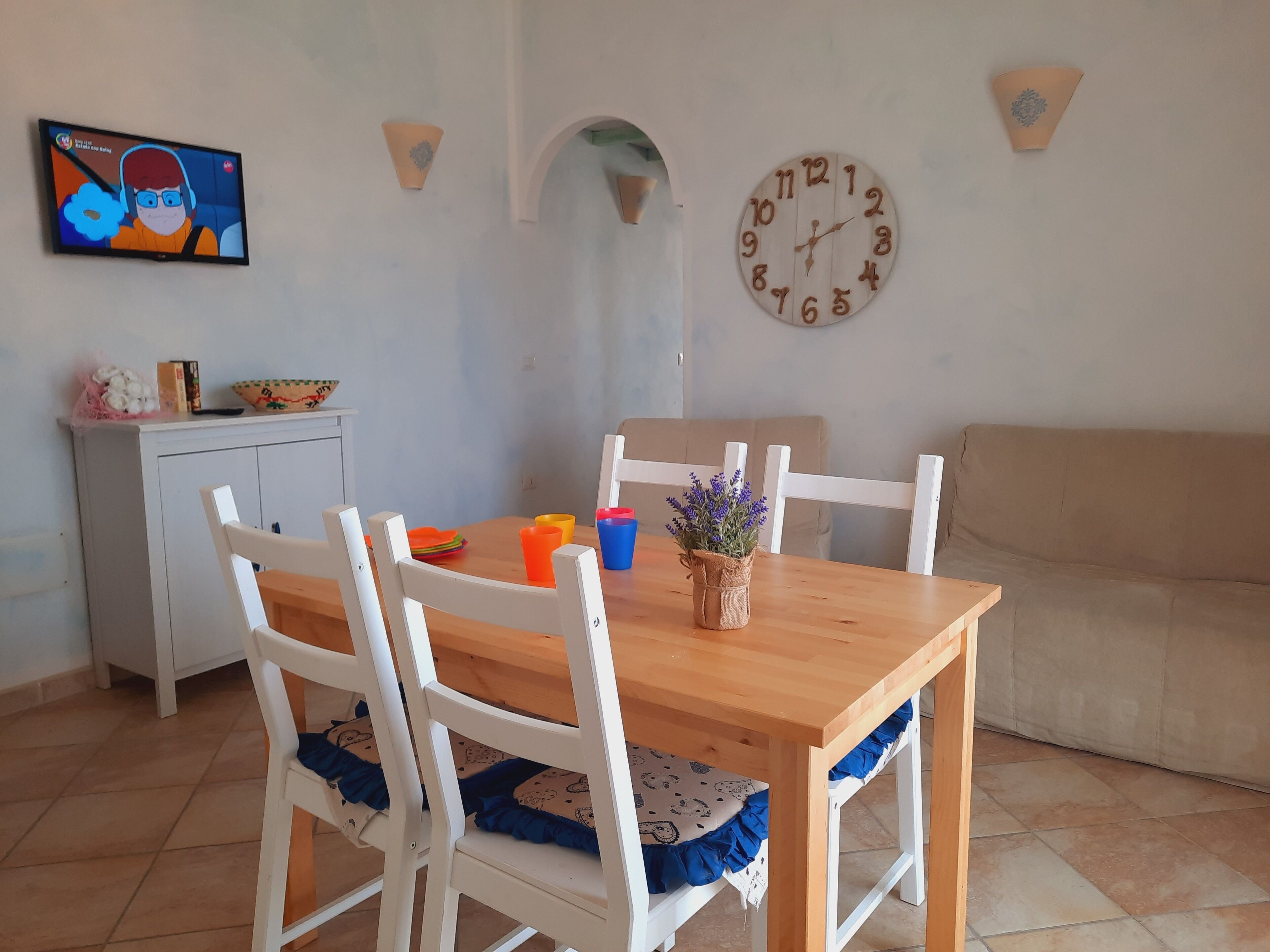 Zona pranzo con tavolo in legno, sedie bianche e divano color beige.