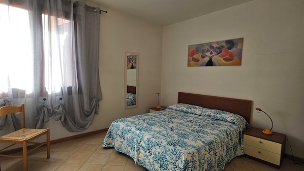 Ein Schlafzimmer mit einem Bett, einem Sessel, einem Nachttisch, einer Lampe, einem Spiegel und einem Bild an der Wand.