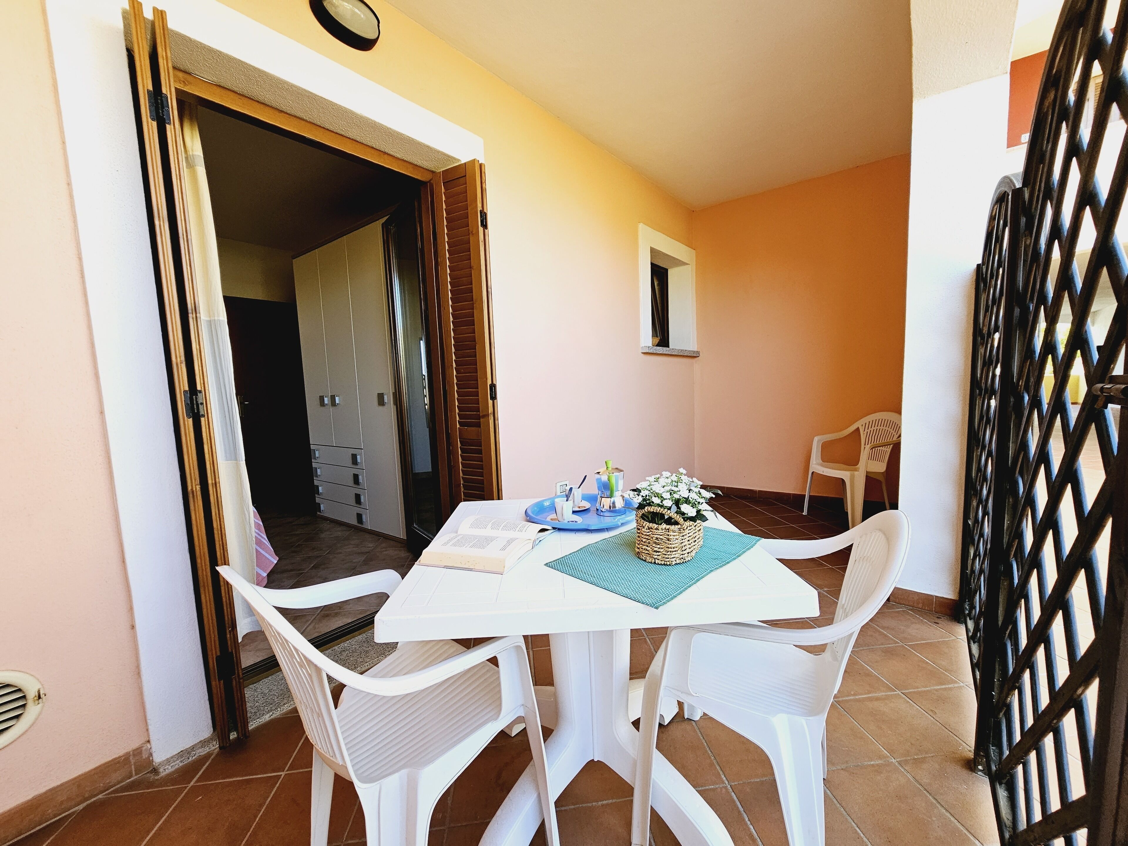 A small dining area with a white table and chairs, a basket of flowers, and a window with a view of the interior.