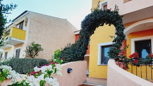 A staircase leading to a building with a yellow facade, surrounded by greenery and flowers. - Appartamenti Santa Teresa Gallura (Santa Teresa di Gallura)