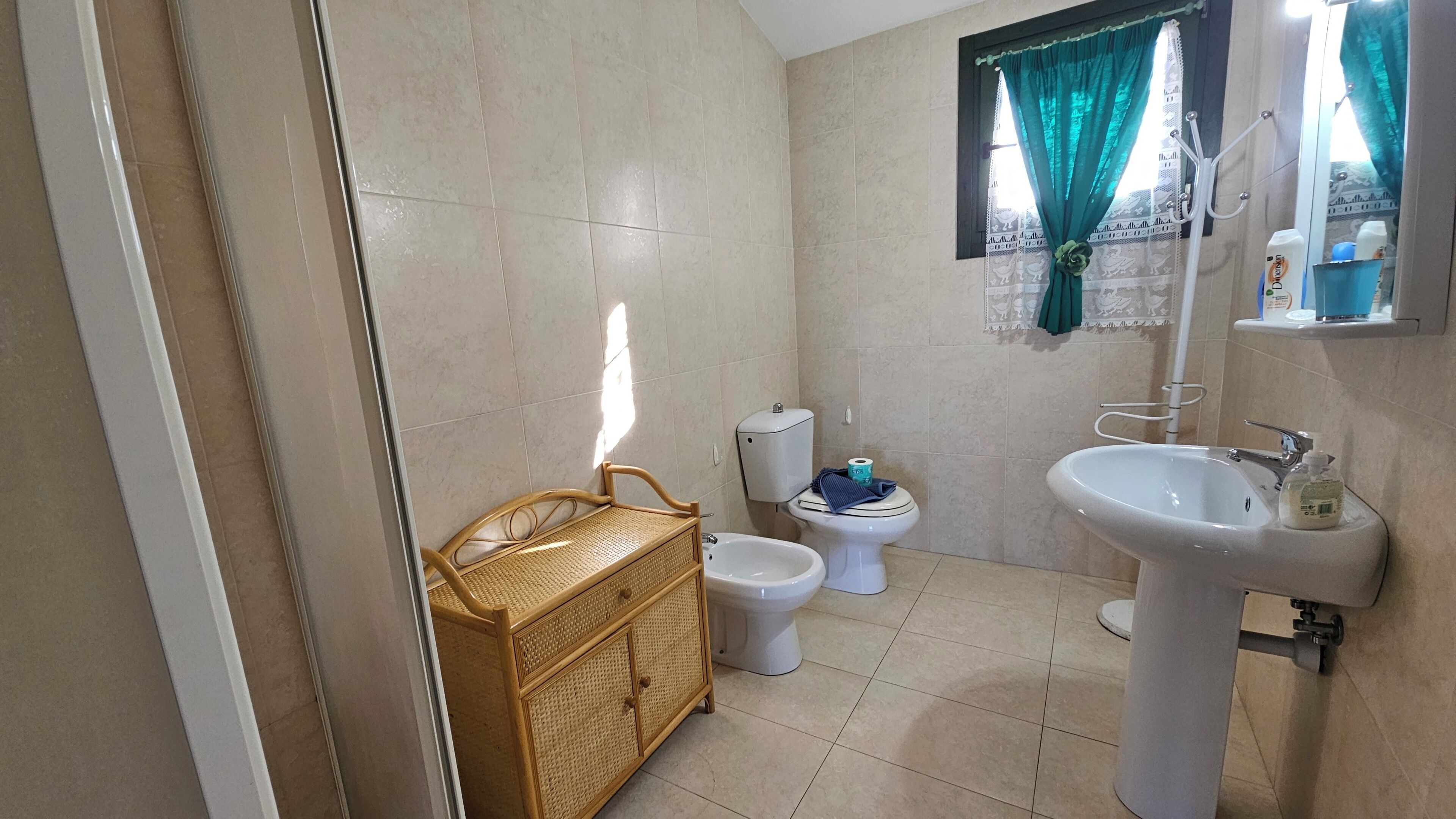 A bathroom with a toilet, bidet, sink, and wicker furniture.
