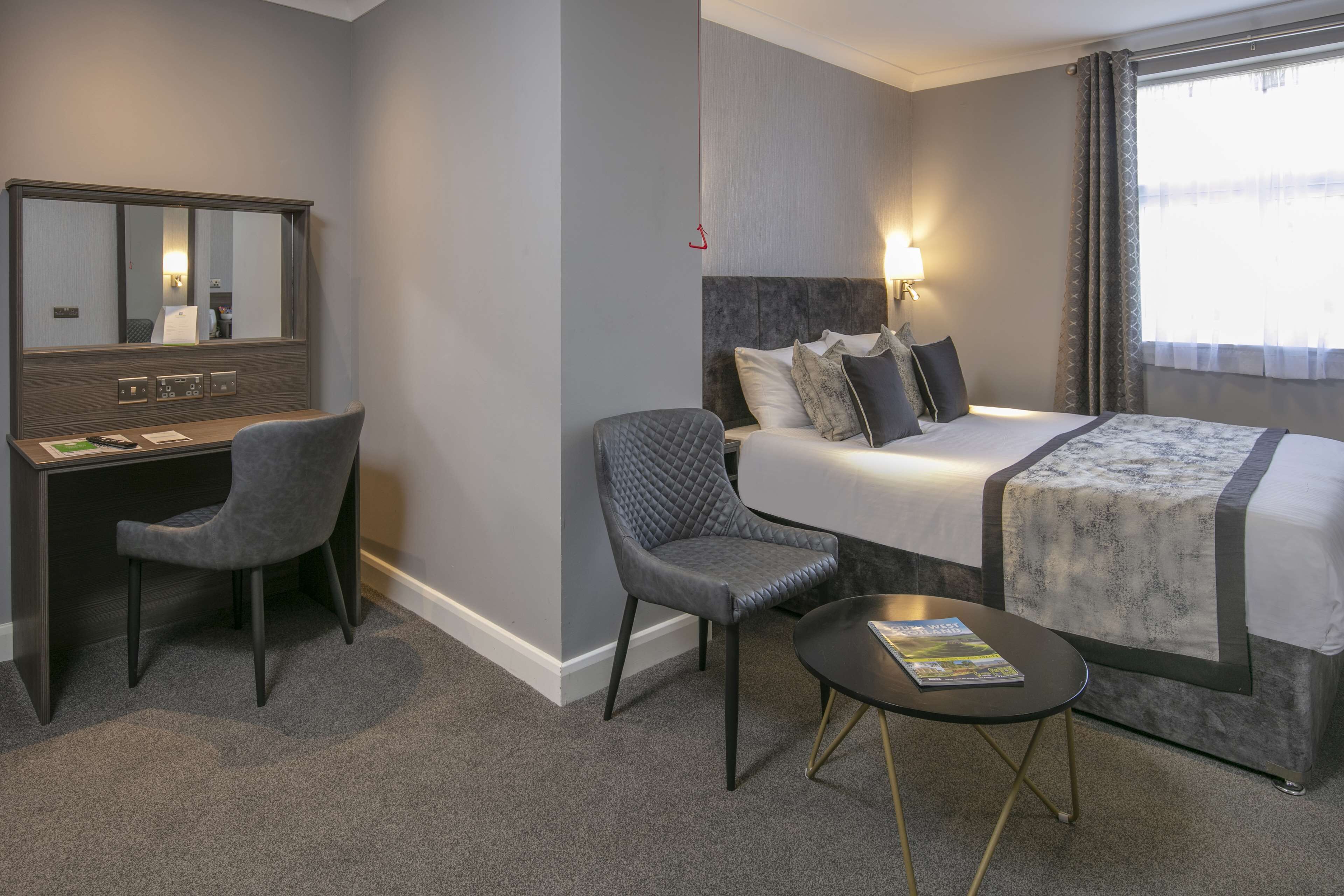 A hotel room with a bed, a desk, a chair, and a small table.