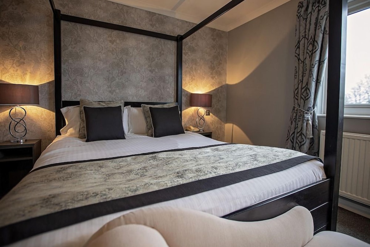 A four-poster bed with a dark frame, two bedside lamps, and a patterned bedspread.