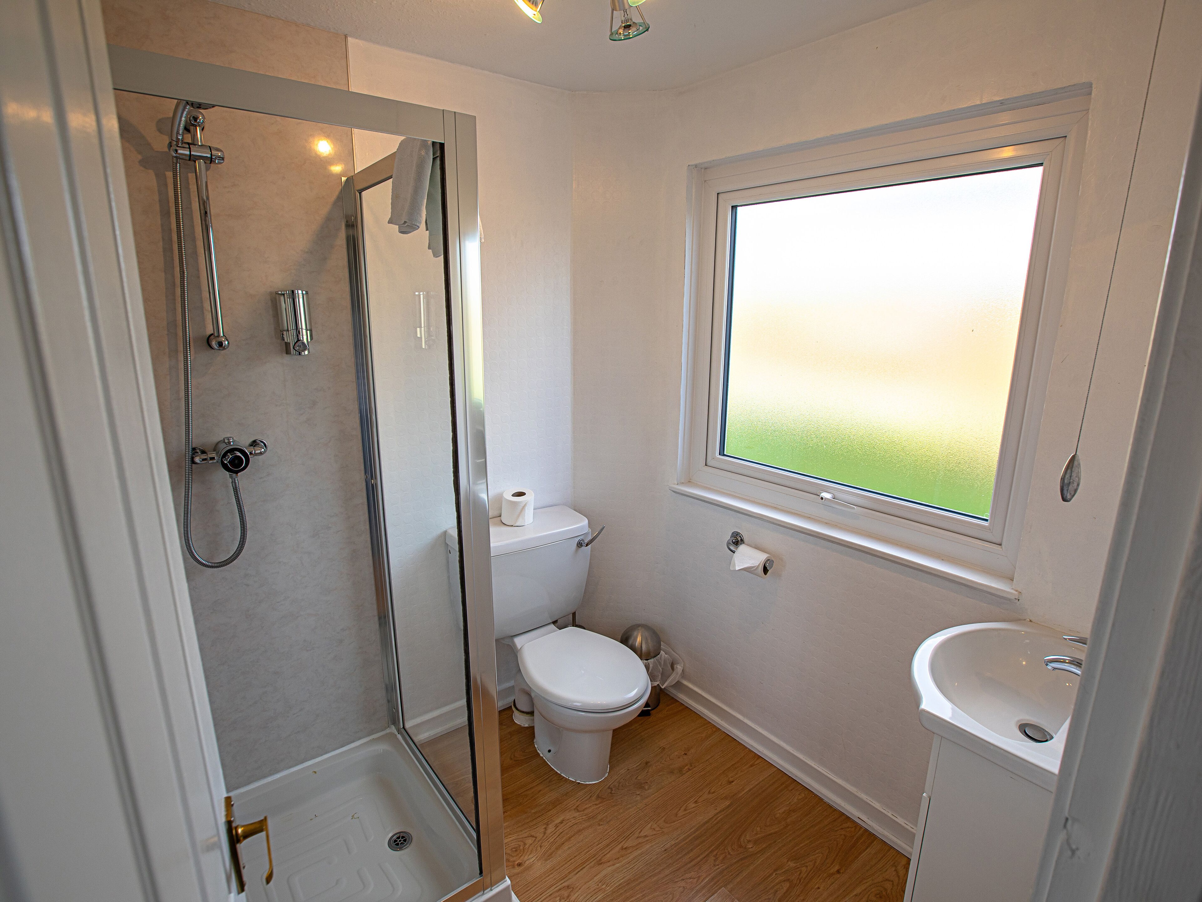 Un baño con ducha, inodoro y lavamanos, que cuenta con una ventana con vistas al exterior.
