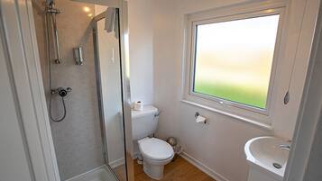 Un baño con ducha, inodoro y lavamanos, que cuenta con una ventana con vistas al exterior.