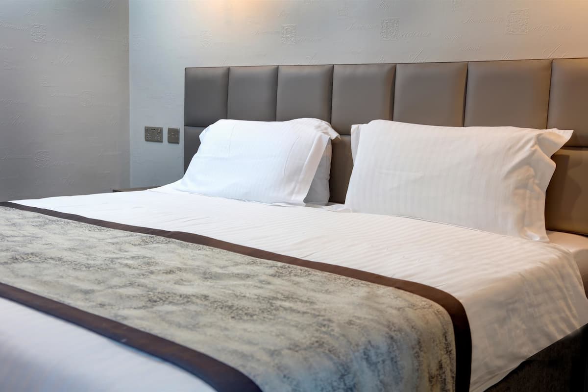 A neatly made bed with white linens and a grey headboard.