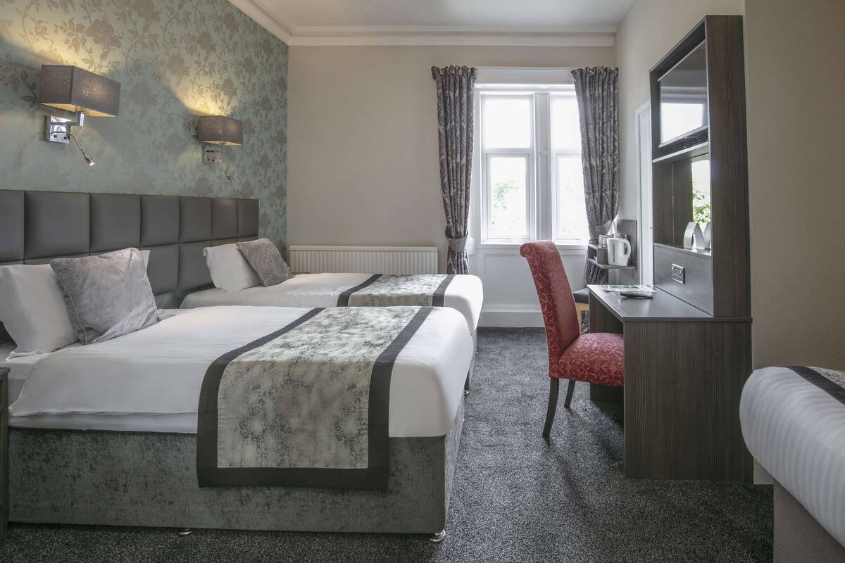 A hotel room with two beds, a desk, a chair, and a large mirror.