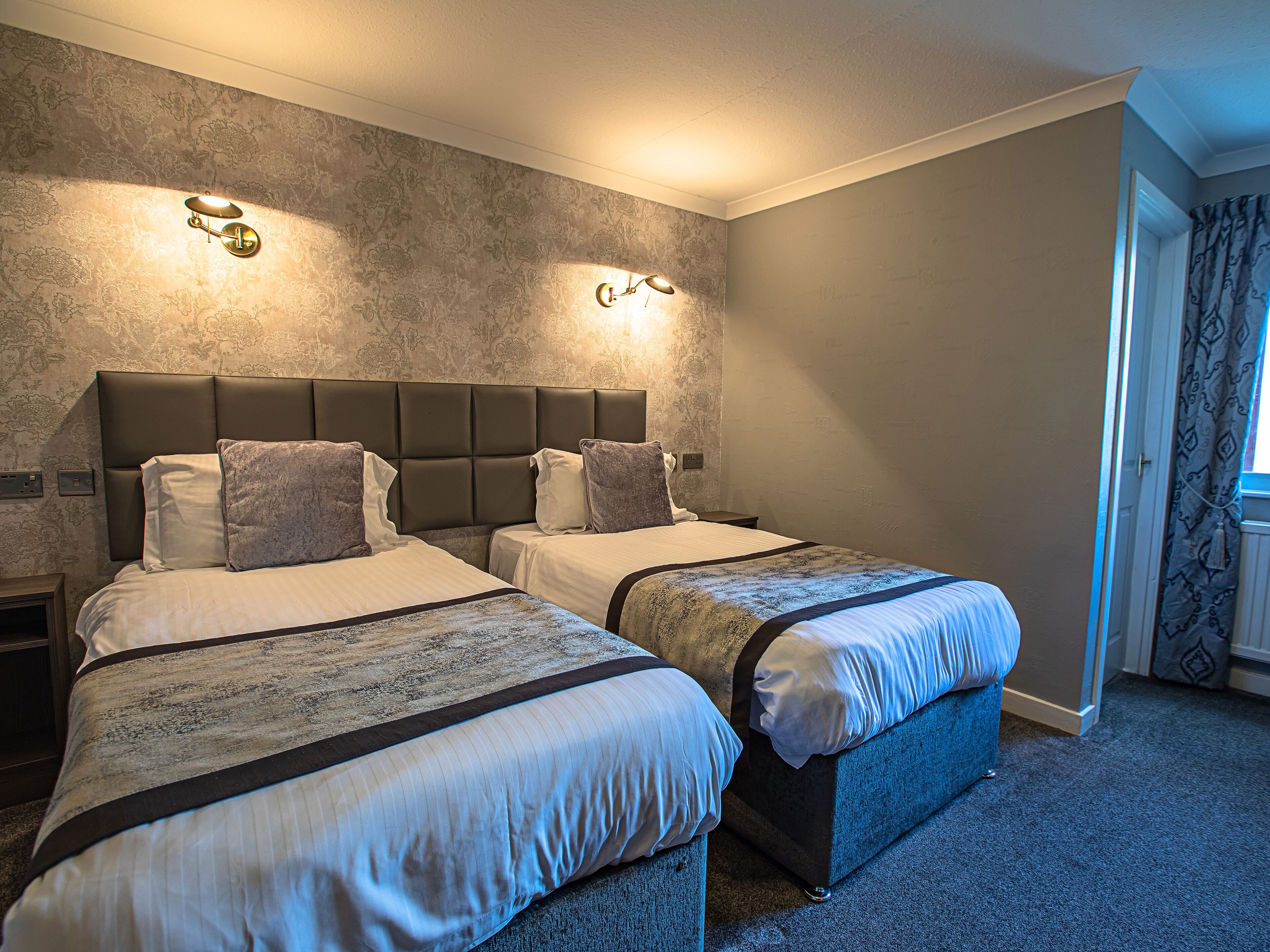 A hotel room with two beds, a dark headboard, and a patterned wall.