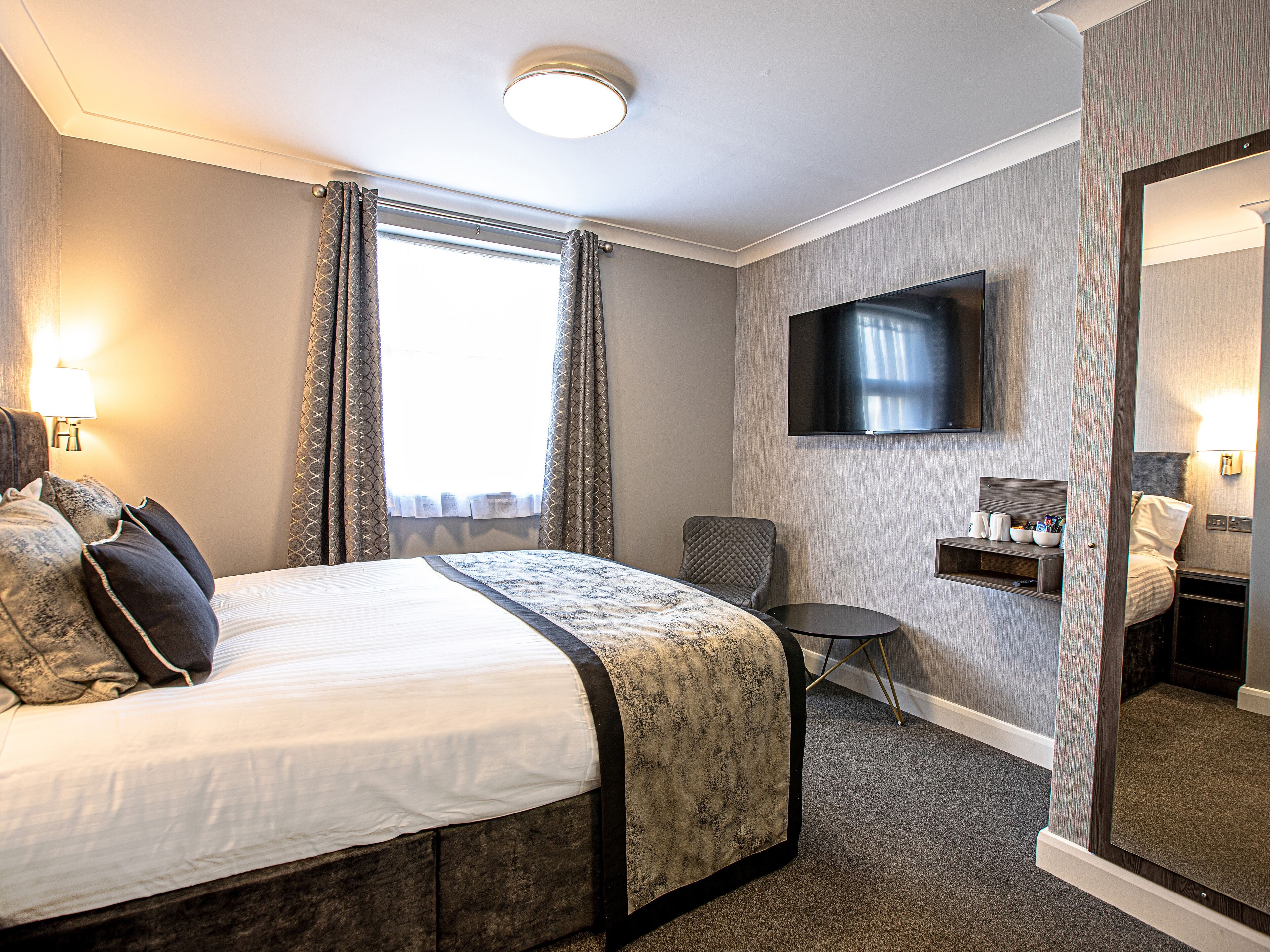 Habitación de hotel con cama, televisor montado en la pared, una mesita y una silla.