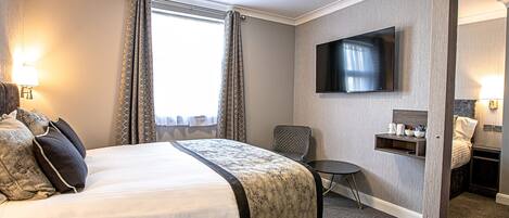 Habitación de hotel con cama, televisor montado en la pared, una mesita y una silla.