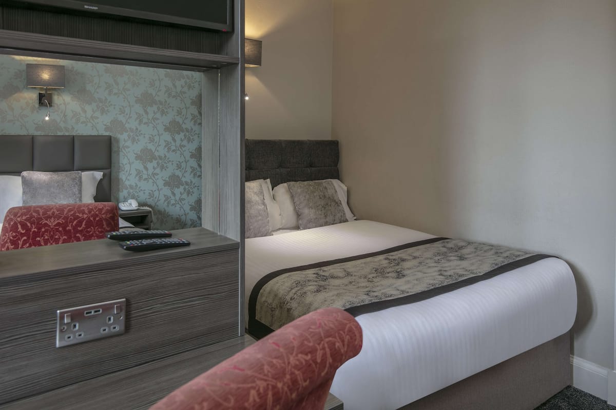 A hotel room with a bed, bedside table, and a mirror.
