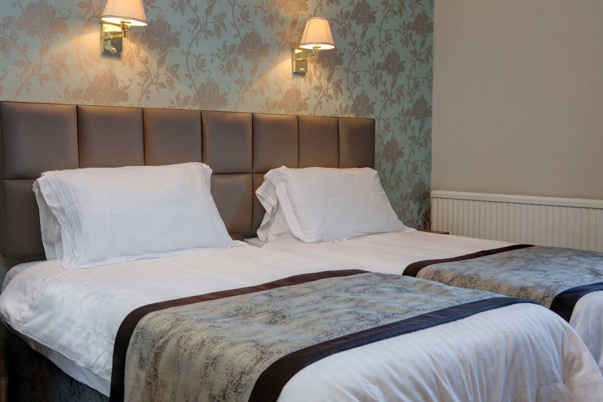 A hotel room with two beds, a padded headboard, and wall-mounted lamps.
