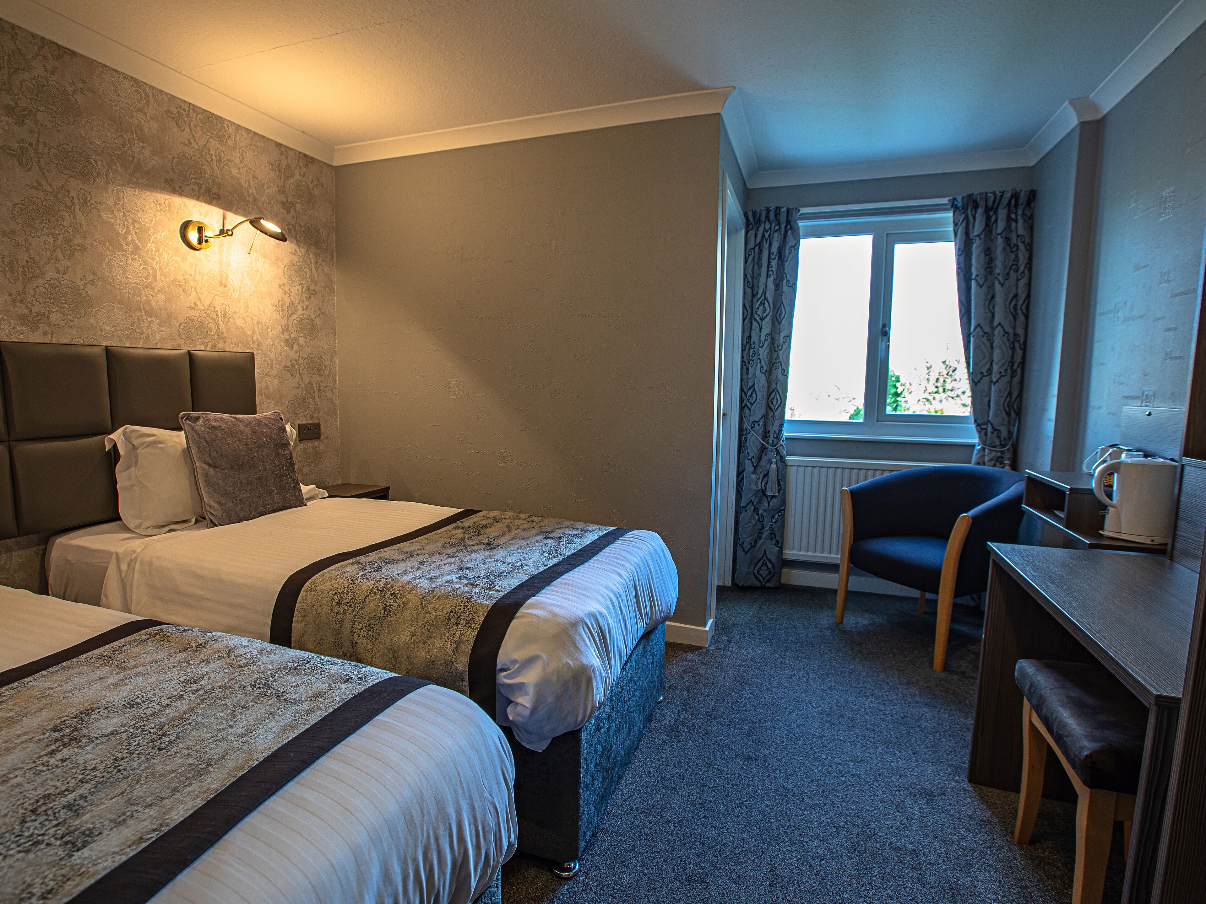 A hotel room with two beds, a desk, and a chair.