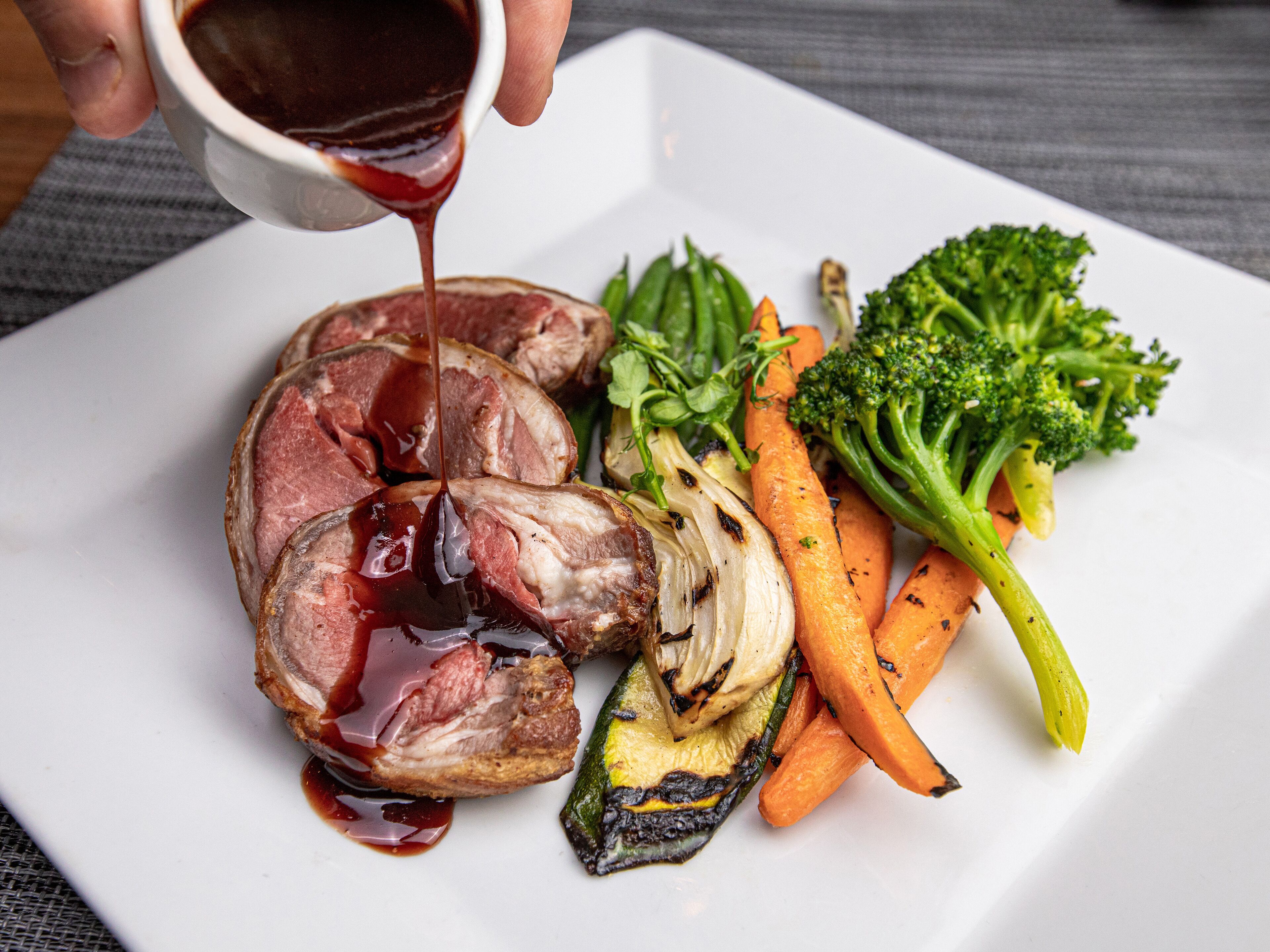 A plate of food with sliced meat, vegetables, and a sauce being poured over it.