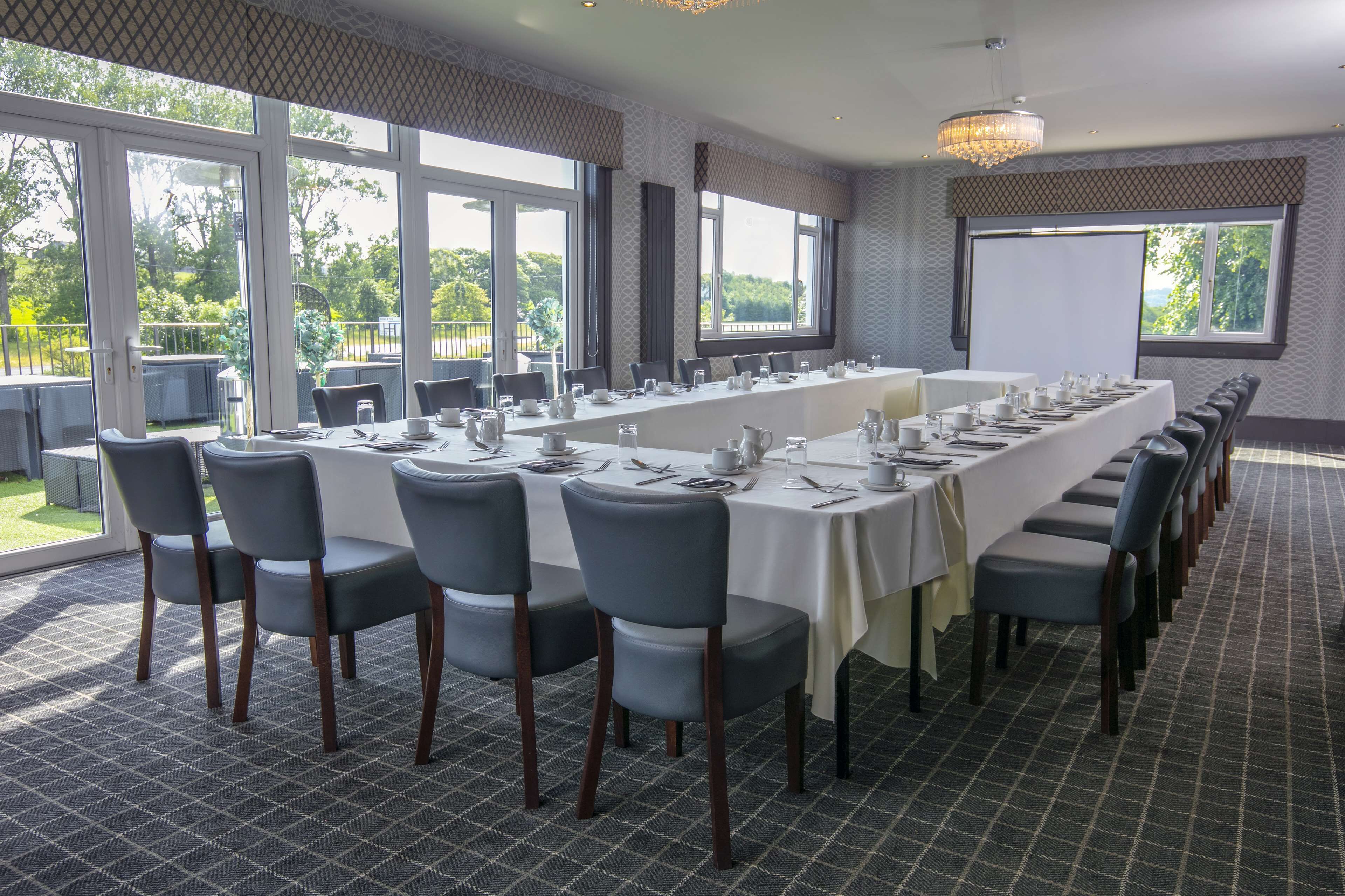 A conference room with a long table set for a meeting, large windows, and a projector screen.