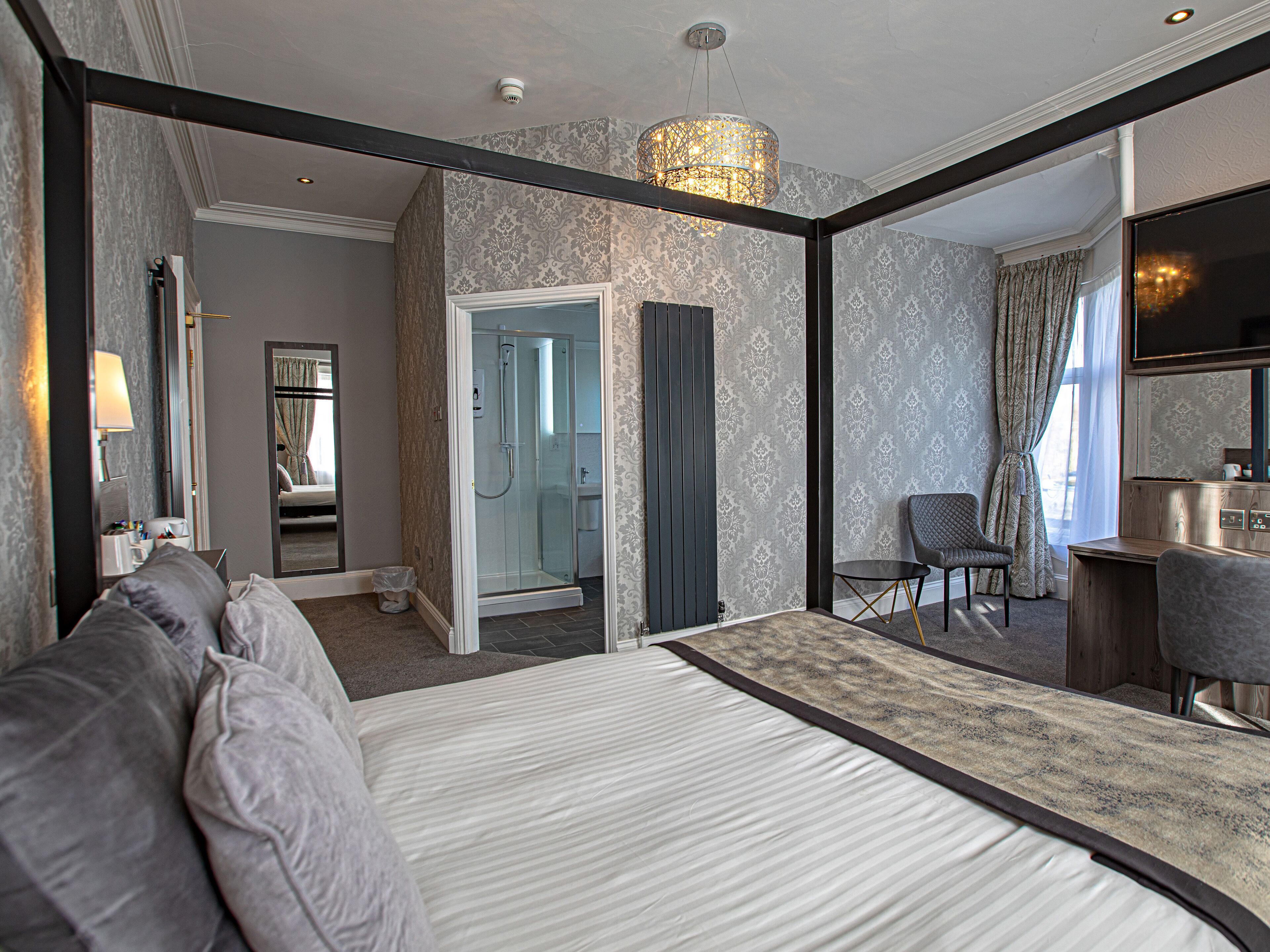 A modern hotel room with a large bed, a shower, a seating area, and a large mirror.