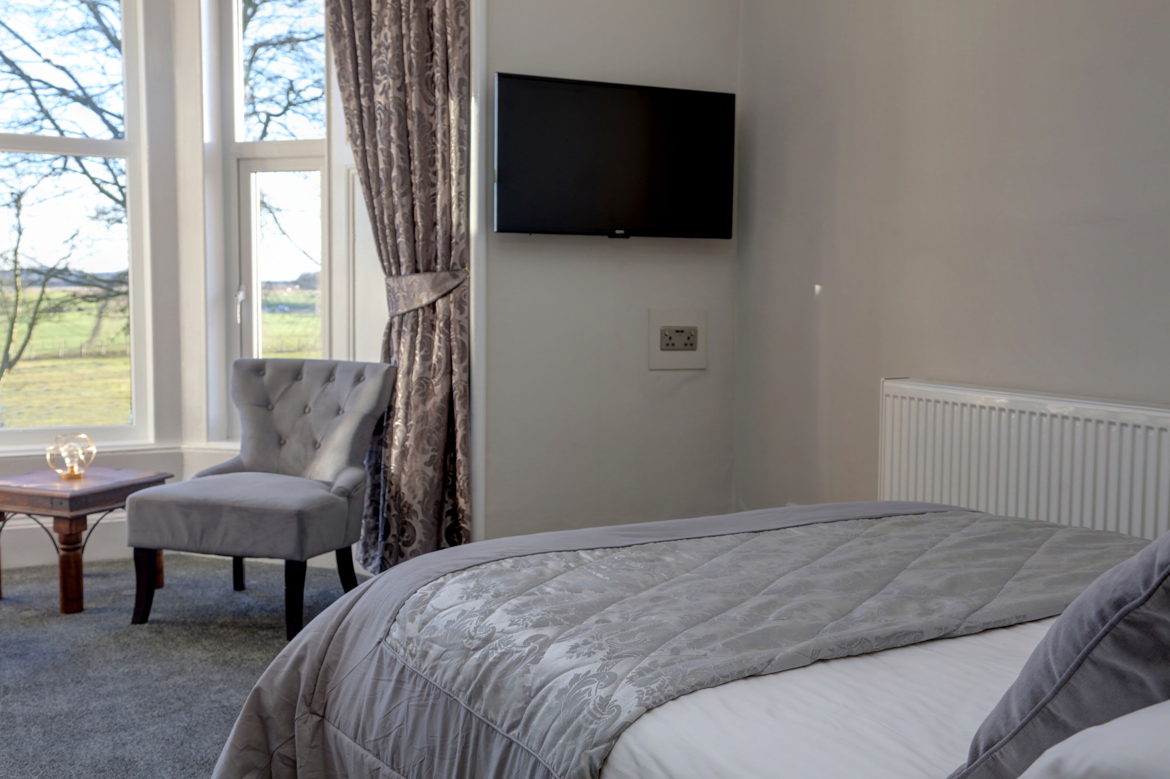 A bedroom with a bed, a chair, a television, and a window with curtains.