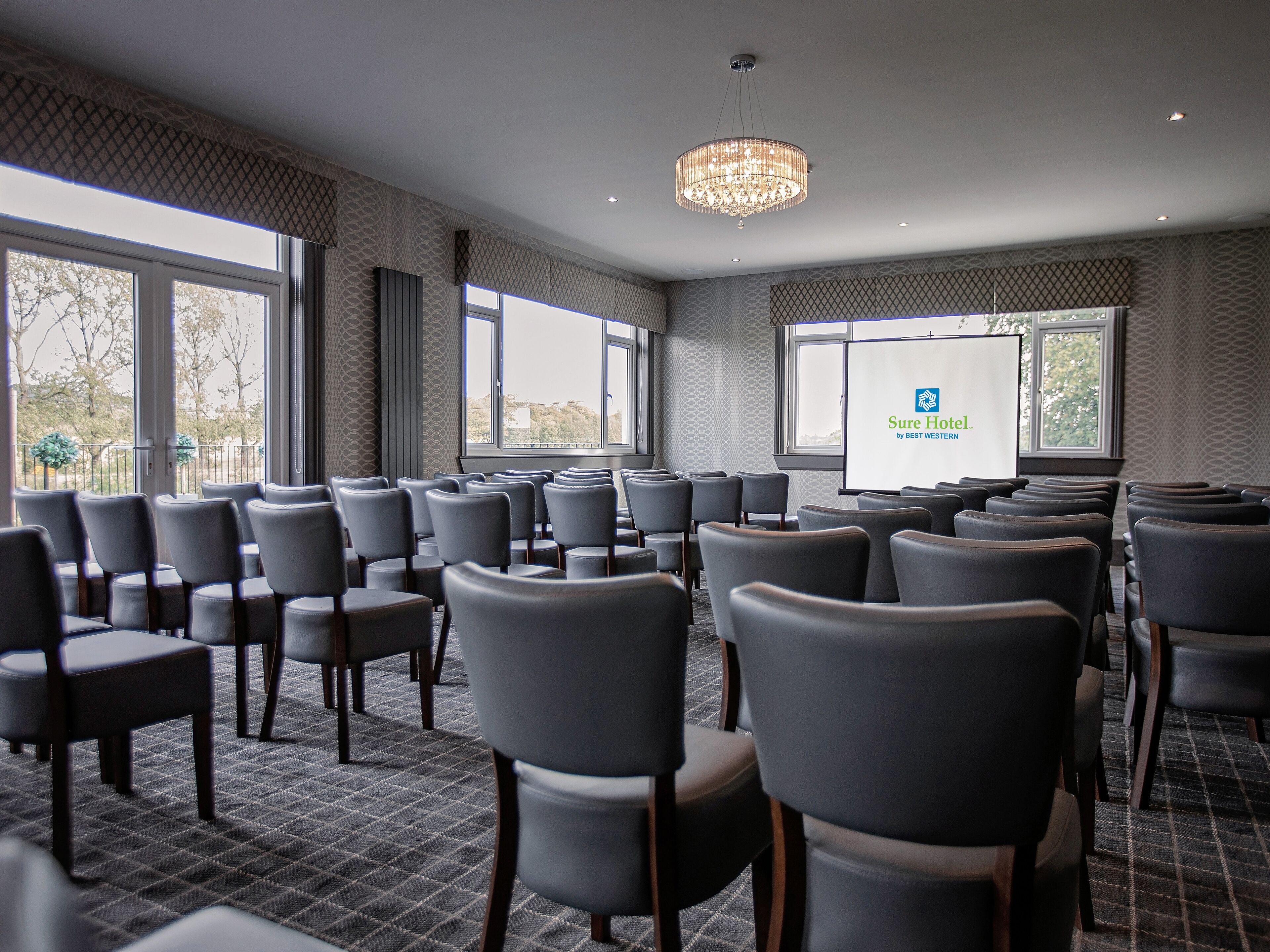 A conference room with rows of chairs facing a projection screen displaying the Sure Hotel logo.