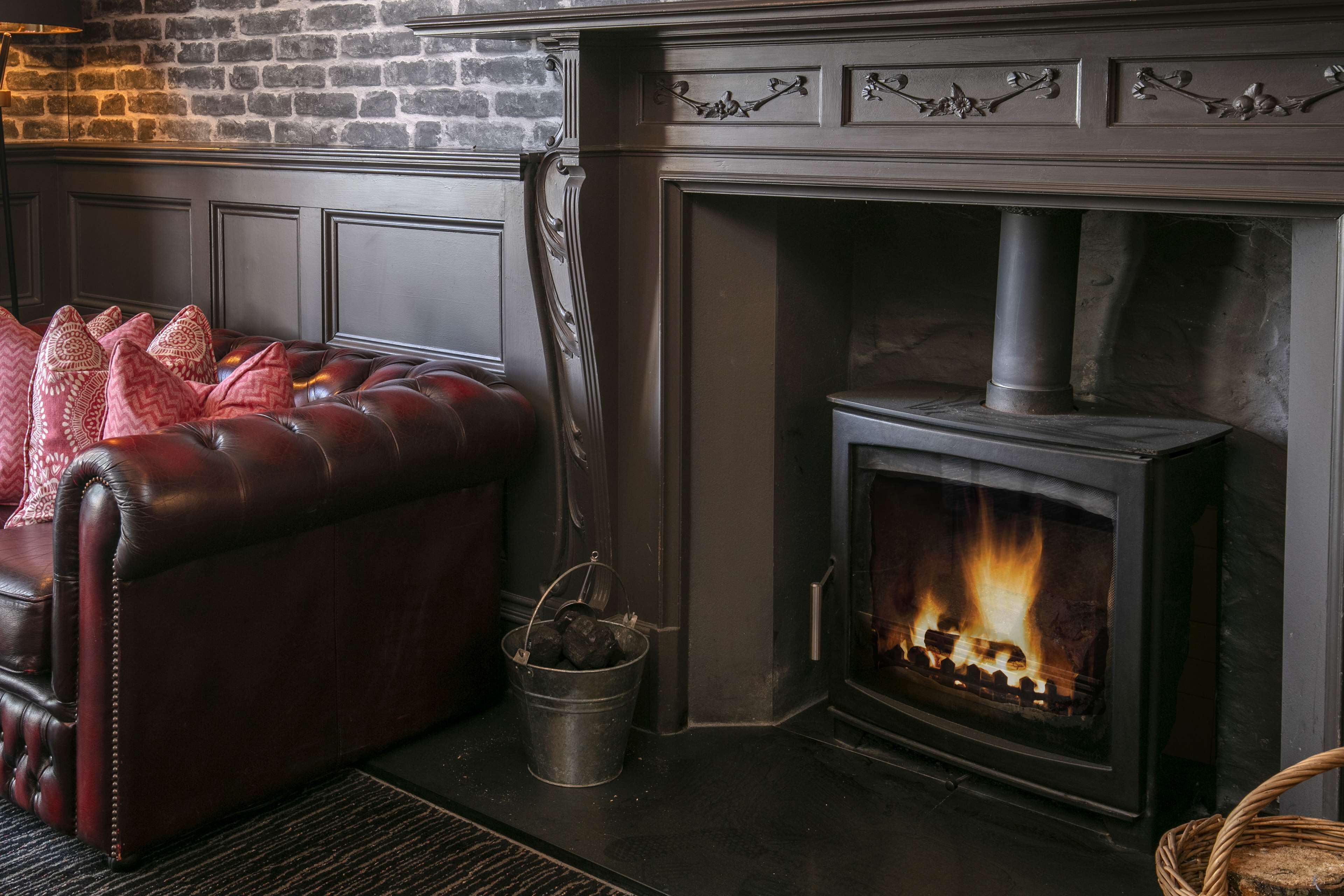 A cozy living room with a leather sofa, a fireplace, and a brick wall.