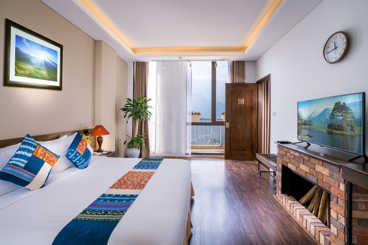 Habitación de hotel con una cama grande, televisión, chimenea y balcón con vistas a las montañas.