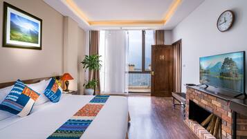A hotel room with a large bed, a television, a fireplace, and a balcony with a view of the mountains.