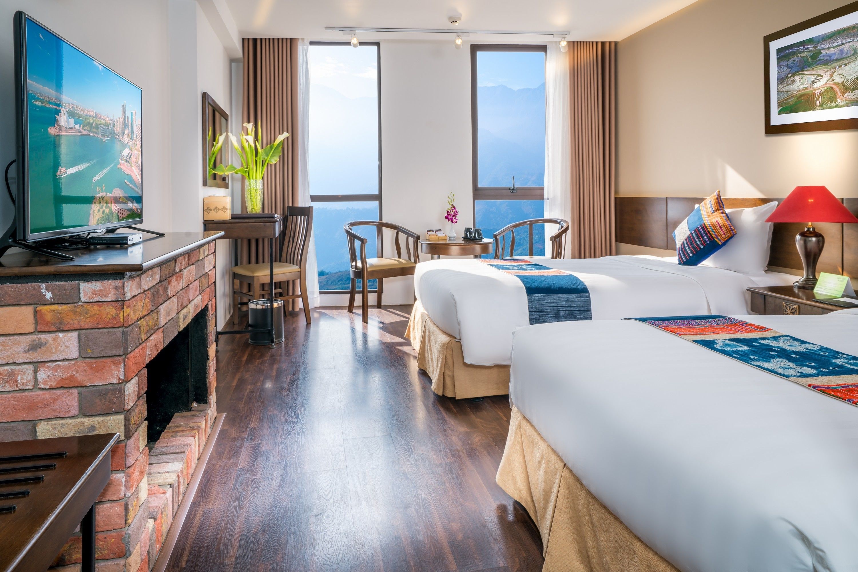 Une chambre d’hôtel équipée d’une télévision, d’une cheminée, de deux lits, d’une table à manger, de chaises et d’une grande fenêtre donnant sur un beau paysage.