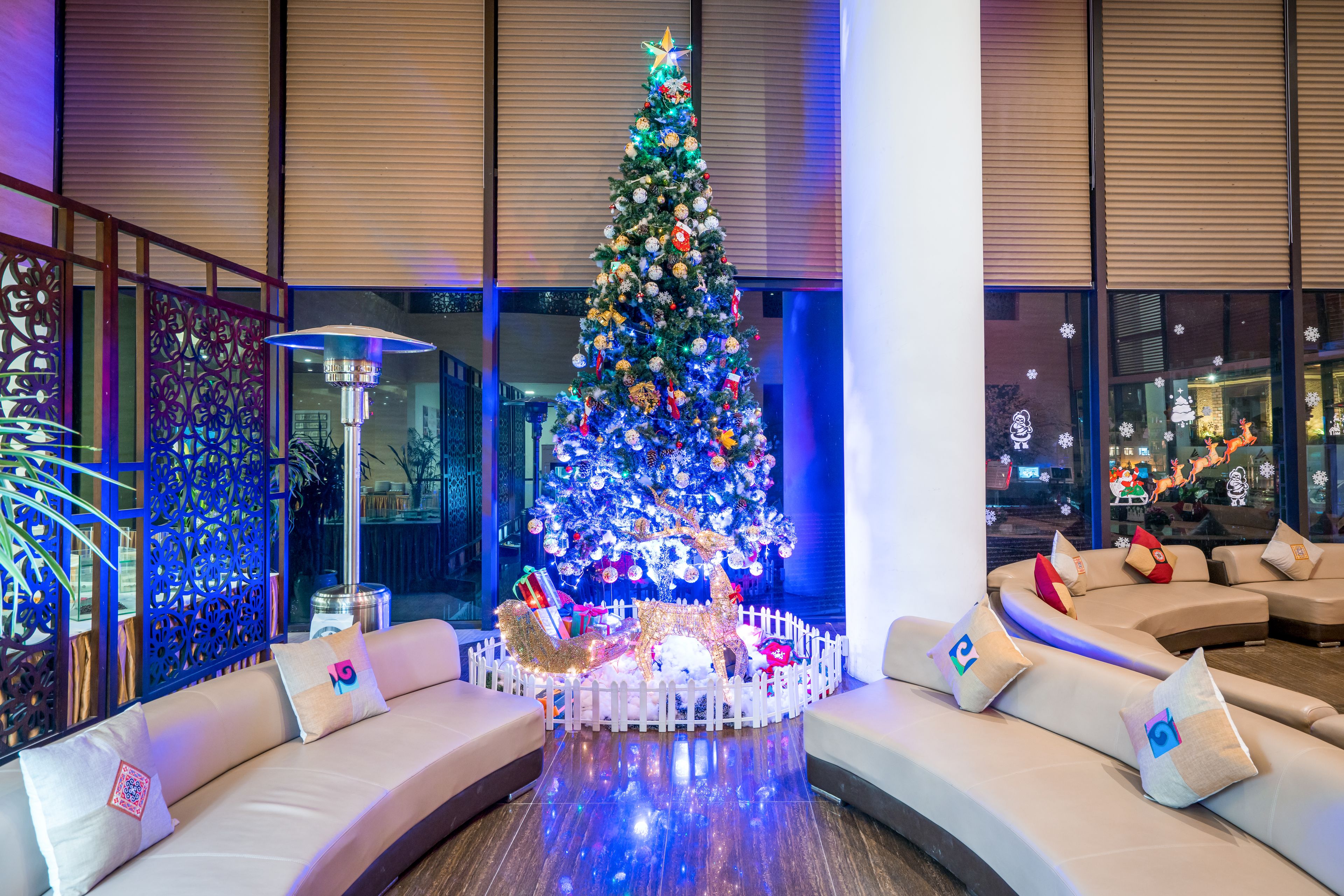 Árbol de Navidad con luces y adornos en un vestíbulo moderno con valla blanca, un sofá y una pared decorativa.