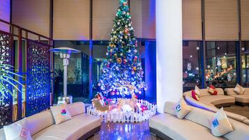 Árbol de Navidad con luces y adornos en un vestíbulo moderno con valla blanca, un sofá y una pared decorativa.