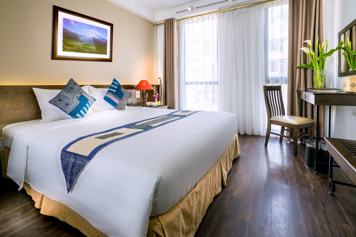 Una habitación de hotel con una cama grande, un escritorio, una silla y un ventanal con cortinas.