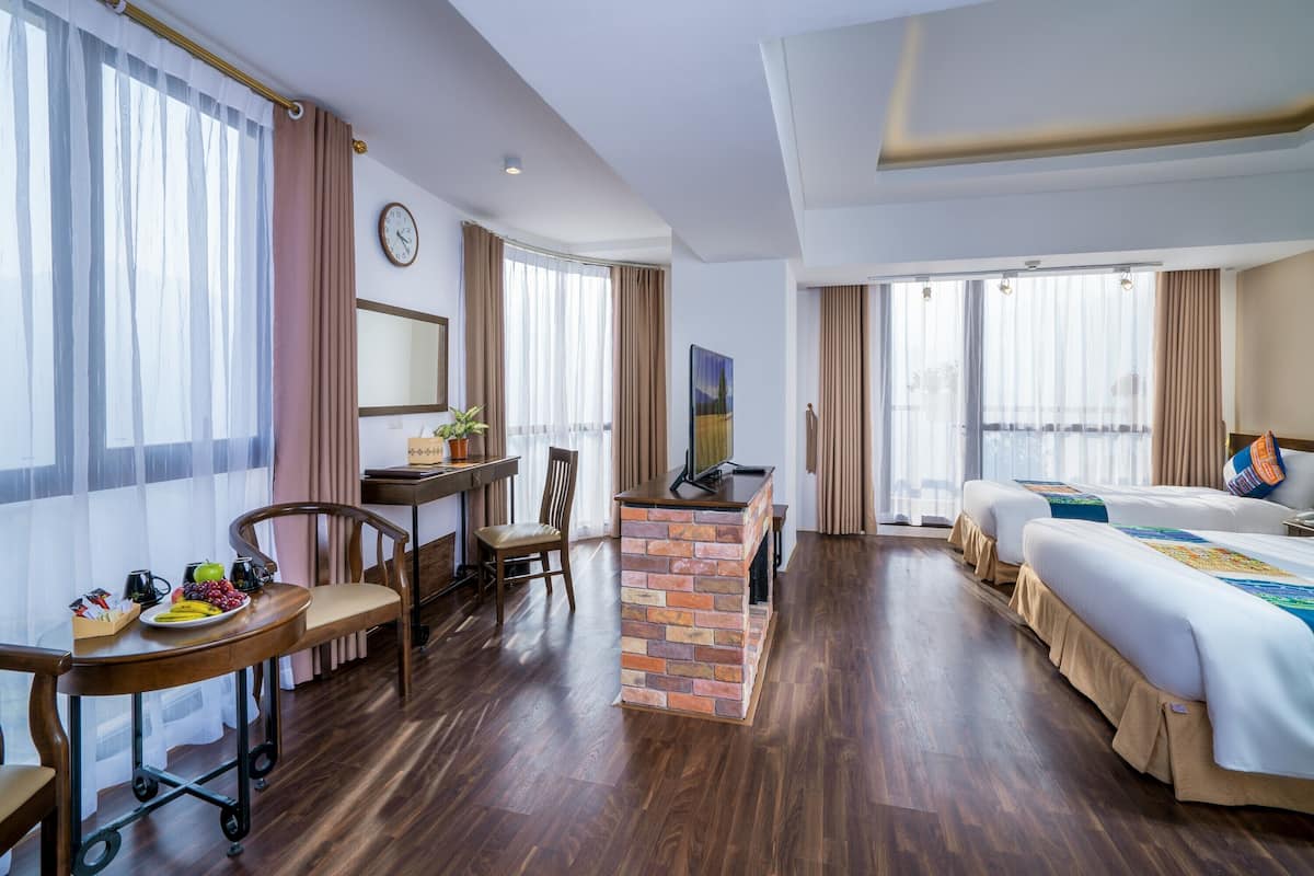 Habitación de hotel con escritorio, sillas, televisor, cama y pared decorativa de ladrillo.