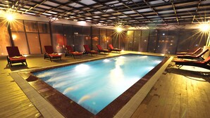 An indoor swimming pool with clear water, surrounded by red lounge chairs and a wooden deck. - Amazing Hotel Sapa (Sa Pa)