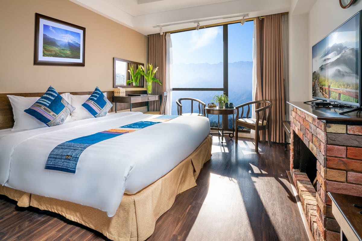 Habitación de hotel con una cama grande, televisión, zona de comedor y vistas a la montaña.