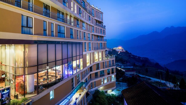 A multi-story hotel with balconies, large windows, and a view of the surrounding landscape. - Amazing Hotel Sapa (Sa Pa)