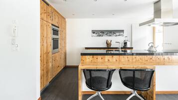 A modern kitchen with wooden cabinetry, a black countertop, and two black mesh chairs.