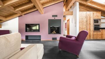 Un soggiorno moderno con soffitto alto, travi in legno, un camino, una televisione e un angolo cottura con pannelli di legno.