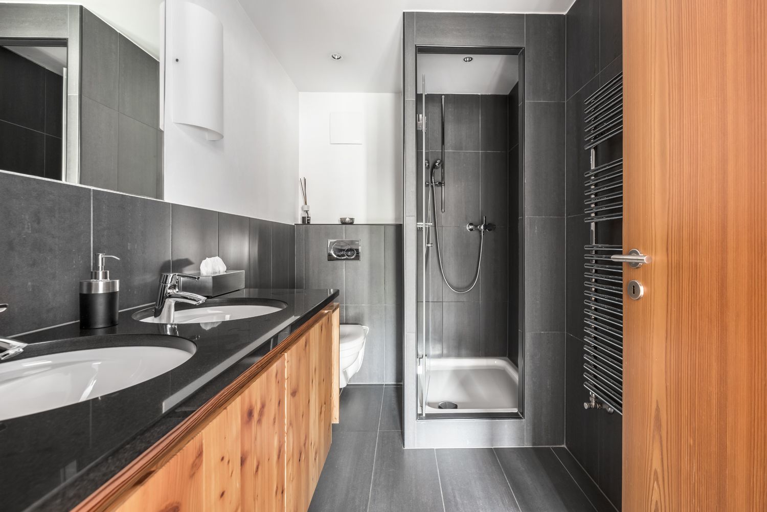 Un baño moderno con dos lavamanos, ducha y tocador de madera.
