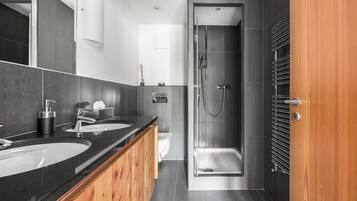 Un baño moderno con dos lavamanos, ducha y tocador de madera.