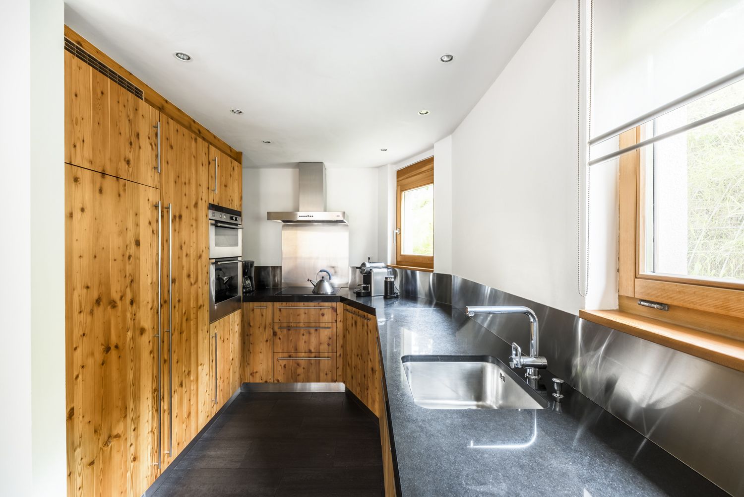 Une cuisine moderne avec des meubles en bois, des appareils électroménagers en acier inoxydable et un plan de travail noir.