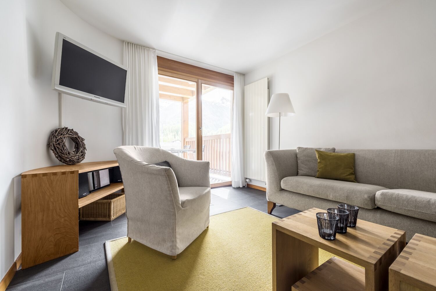 A modern living room with a sofa, armchair, and a flat-screen TV mounted on the wall.