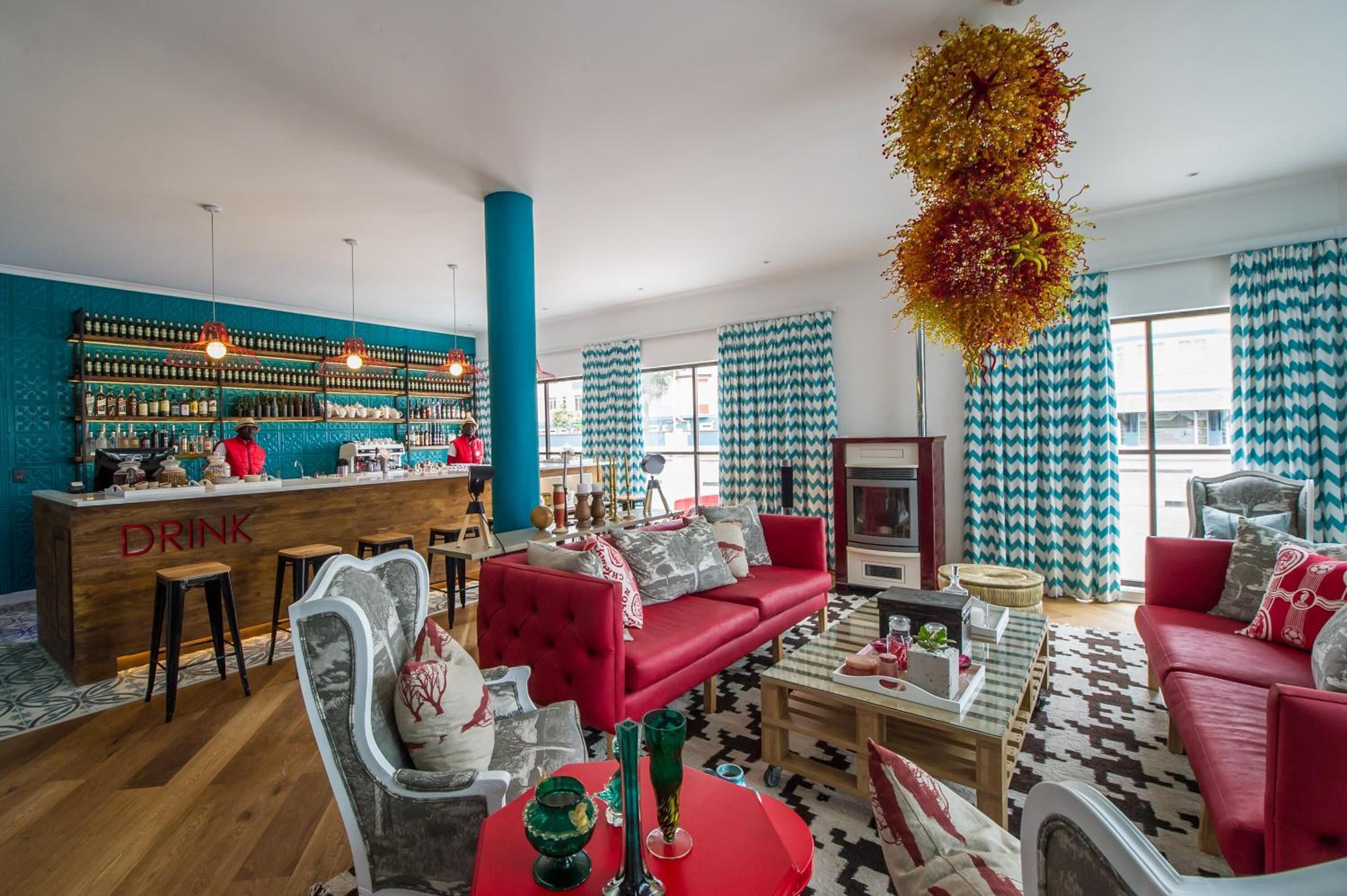 Un espace bar moderne avec un comptoir et des tabourets en bois, un canapé rouge et des rideaux à motifs.