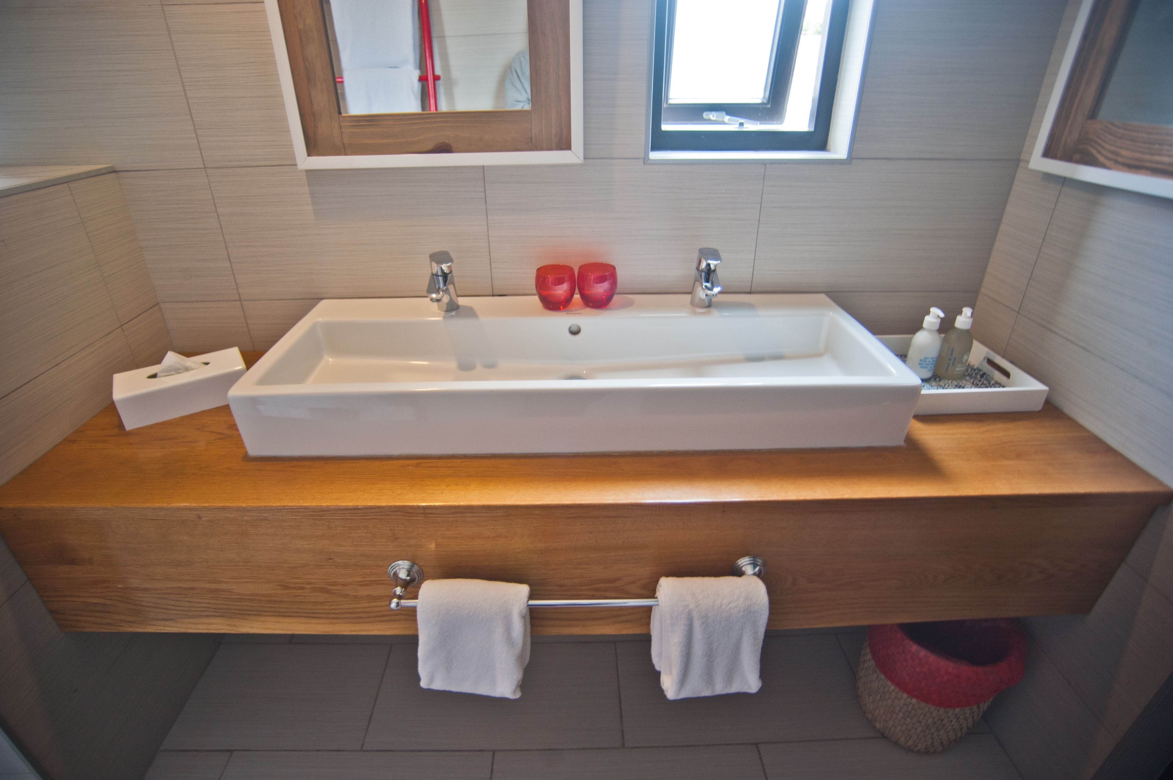 Un bagno moderno con un mobile vanità in legno, un ampio lavabo rettangolare, due saponette rosse e uno specchio sopra il lavabo.