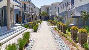 Un immeuble résidentiel moderne doté d’un chemin central bordé de jardinières et de verdure.
