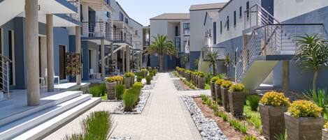 Un moderno edificio residencial con un camino central bordeado por jardineras y follaje.