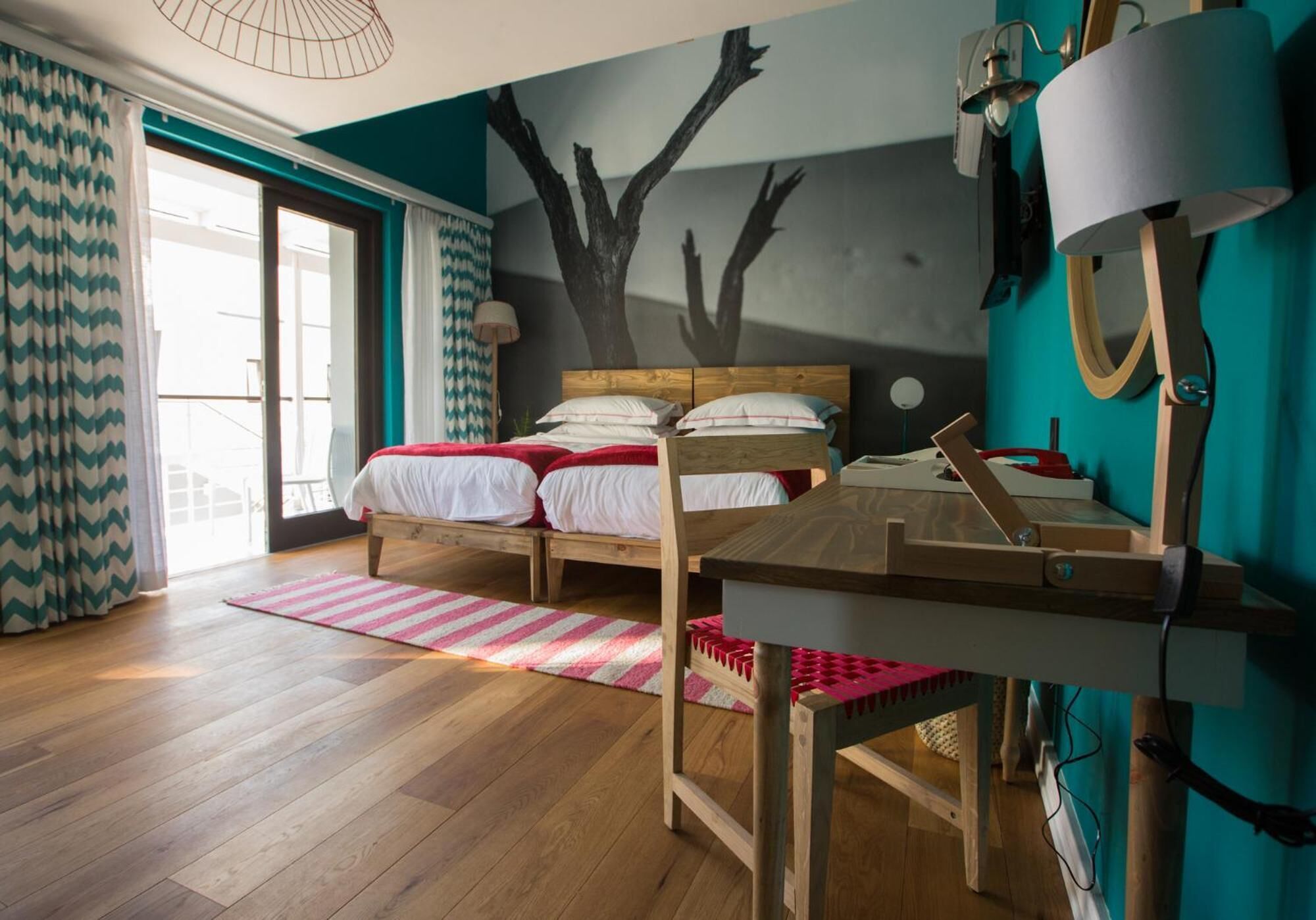 Un dormitorio con cama, escritorio, lámpara y vista al exterior.